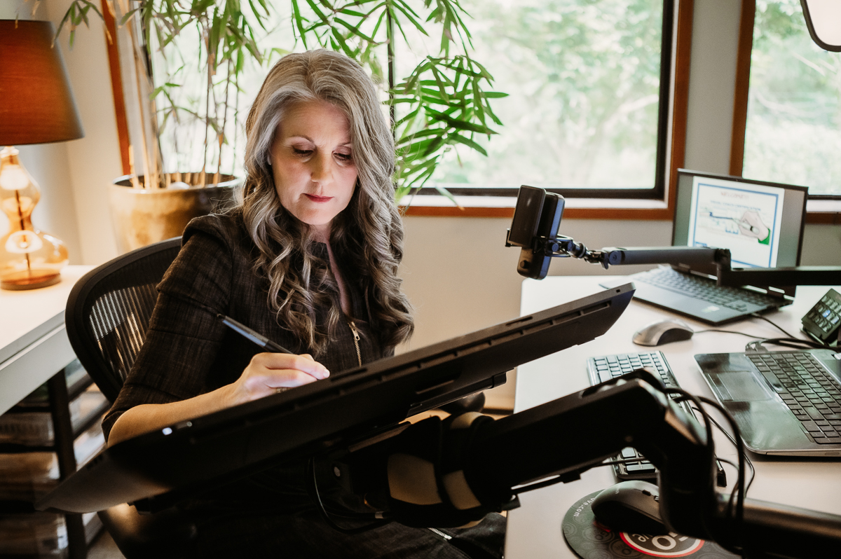 Christina Merkley working at her tablet sketching in her office surounded by technology