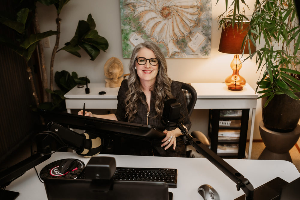 Christina Merkley working at her tablet sketching in her office surounded by technology and plants