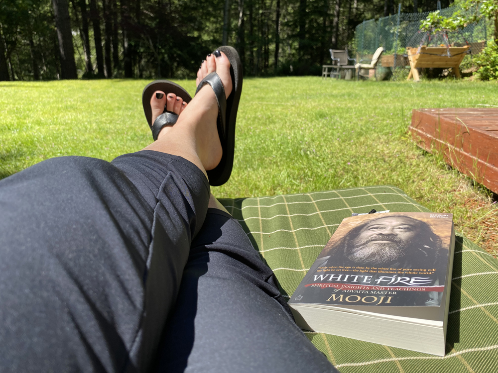 Christina merkley's feet up in her Metchosin BC woods backyard. Taking a break with a book - White Fire. Trees in the background and wide lawn