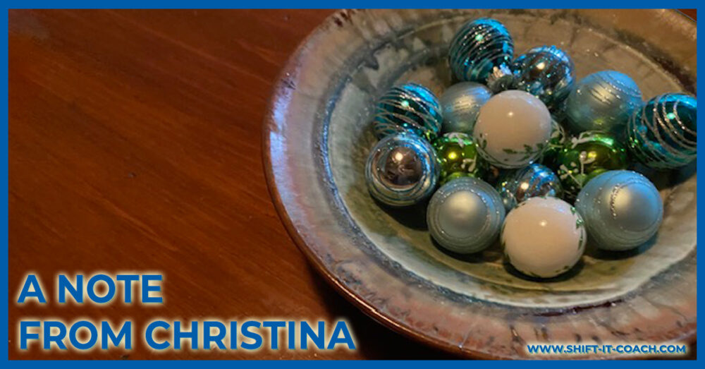 A Note From Christina eZine header featuring a handmade close up of a ceramic bowl filled with sparkling christmas tree balls in blues, golds and silvers on a rich wood desktop
