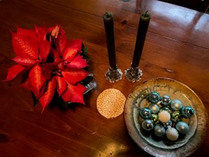 table top with pointsettia, two candelsticks and a bowl of shiny christmas tree balls