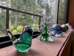 window ledge looking out into the rainforest and hosting green glass bird, balls and a glass christmas tree