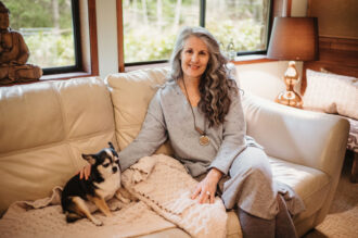 Christina Merkley sitting on the couch with her puppy Presley smiling at the camera.