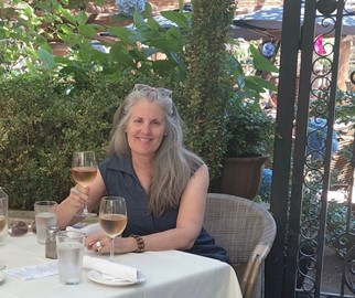 Christina enjoying a glass of wine at a small table outside in the summer's greenery