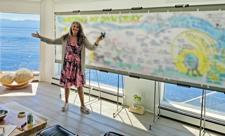 Christina a a visual map board in a sunlit room, surrounded by large windows opening to the sea.