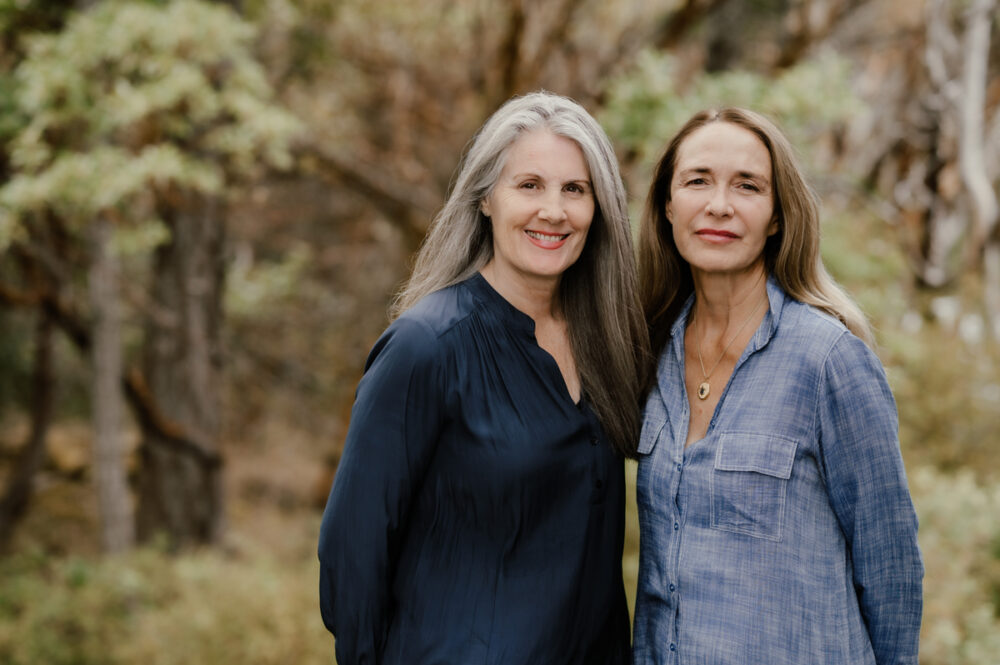 Anneke Lucas and Christina Merkley in Victoria BC smiling at the camera with the rainforest as a backdrop